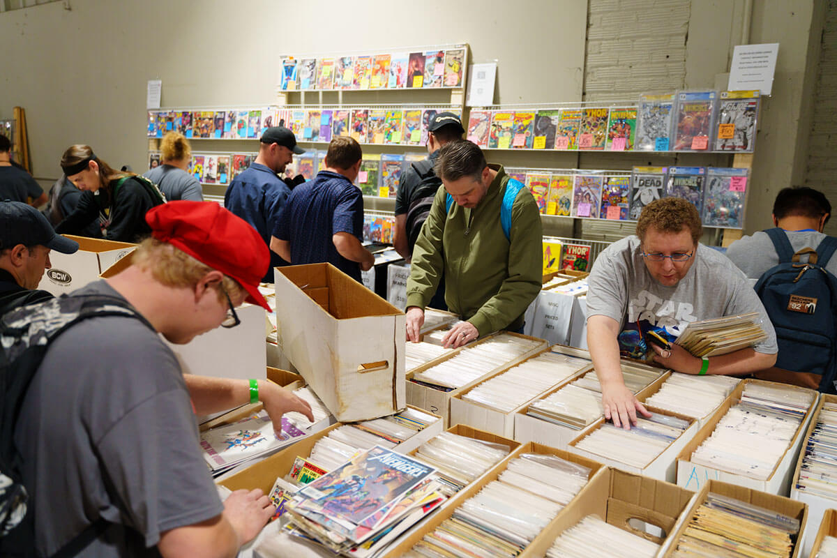 Attendees shopping at one of the MNCBA FallCon 2024 vendors. Photo by Buzz Meade. a small crowd of attendees searching for comic books among tables filled with shortboxes