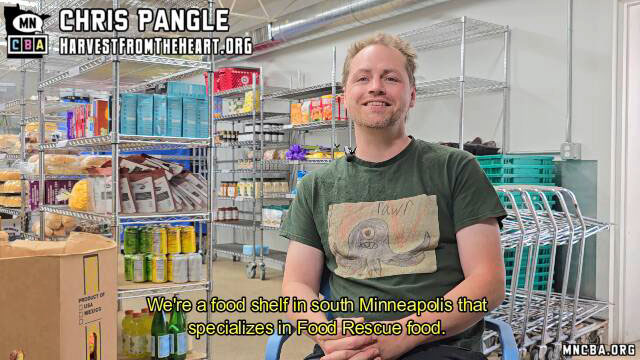 Interview with Chris Pangle, Harvest from the Heart Chris Pangle wearing a green T-shirt, sitting on a chair inside of a food bank designed to resemble a grocery store.